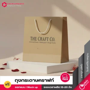 ถุงกระดาษคราฟท์สีน้ำตาลอ่อนมีหูหิ้วเชือกสีขาวสำหรับแบรนด์ THE CRAFT CO. วางอยู่บนแท่นสีขาวในสตูดิโอถ่ายภาพ